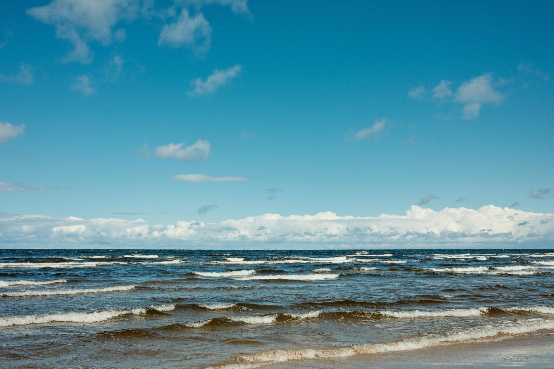 Ocean waves with a clear blue sky and a few clouds.
