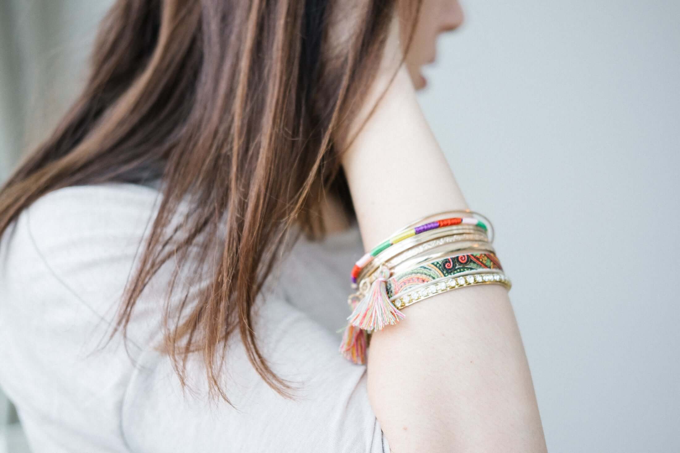Person wearing colorful bracelets on a plain background
