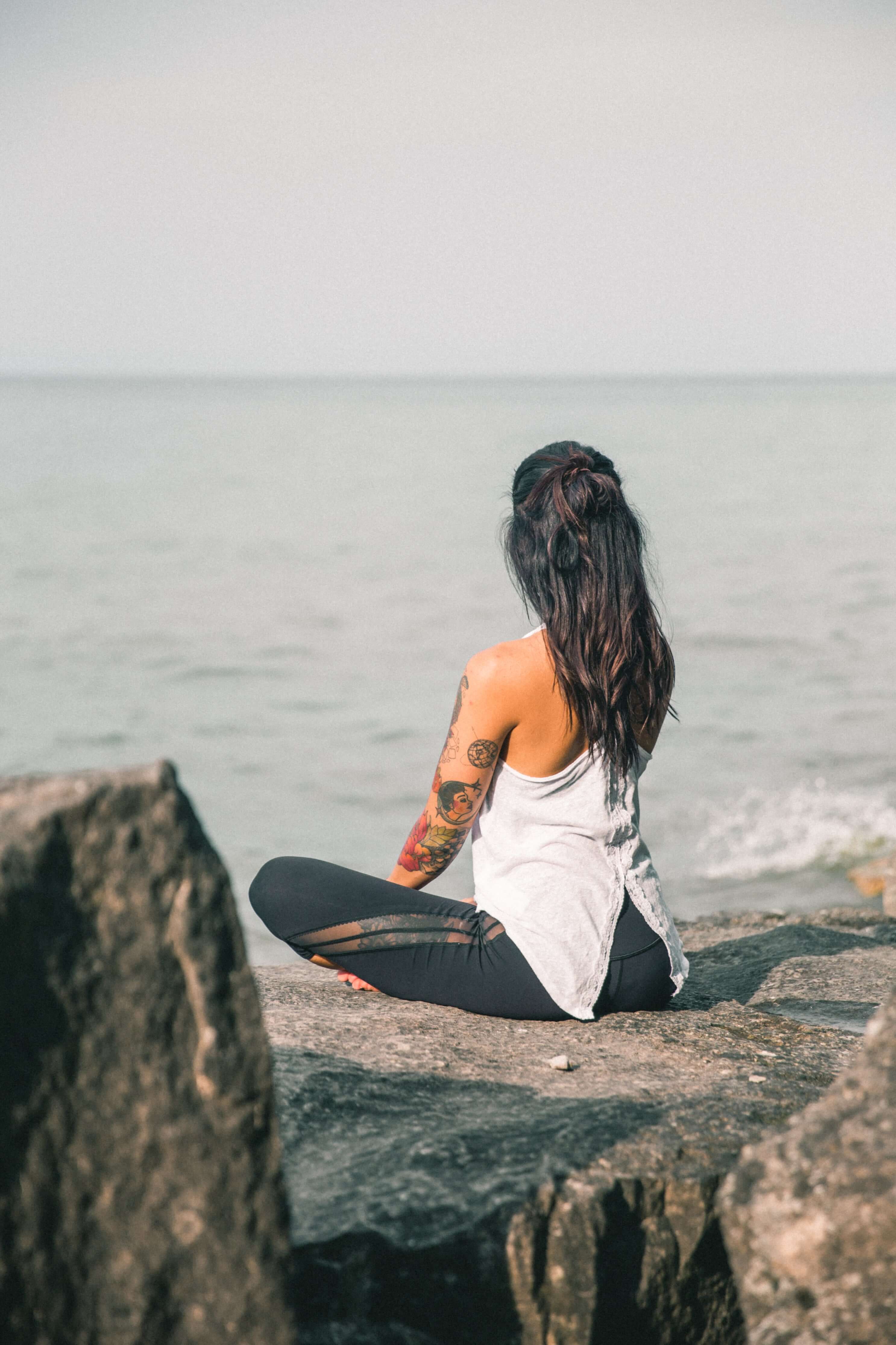 Person sitting on a rock by the ocean with a blurred background
