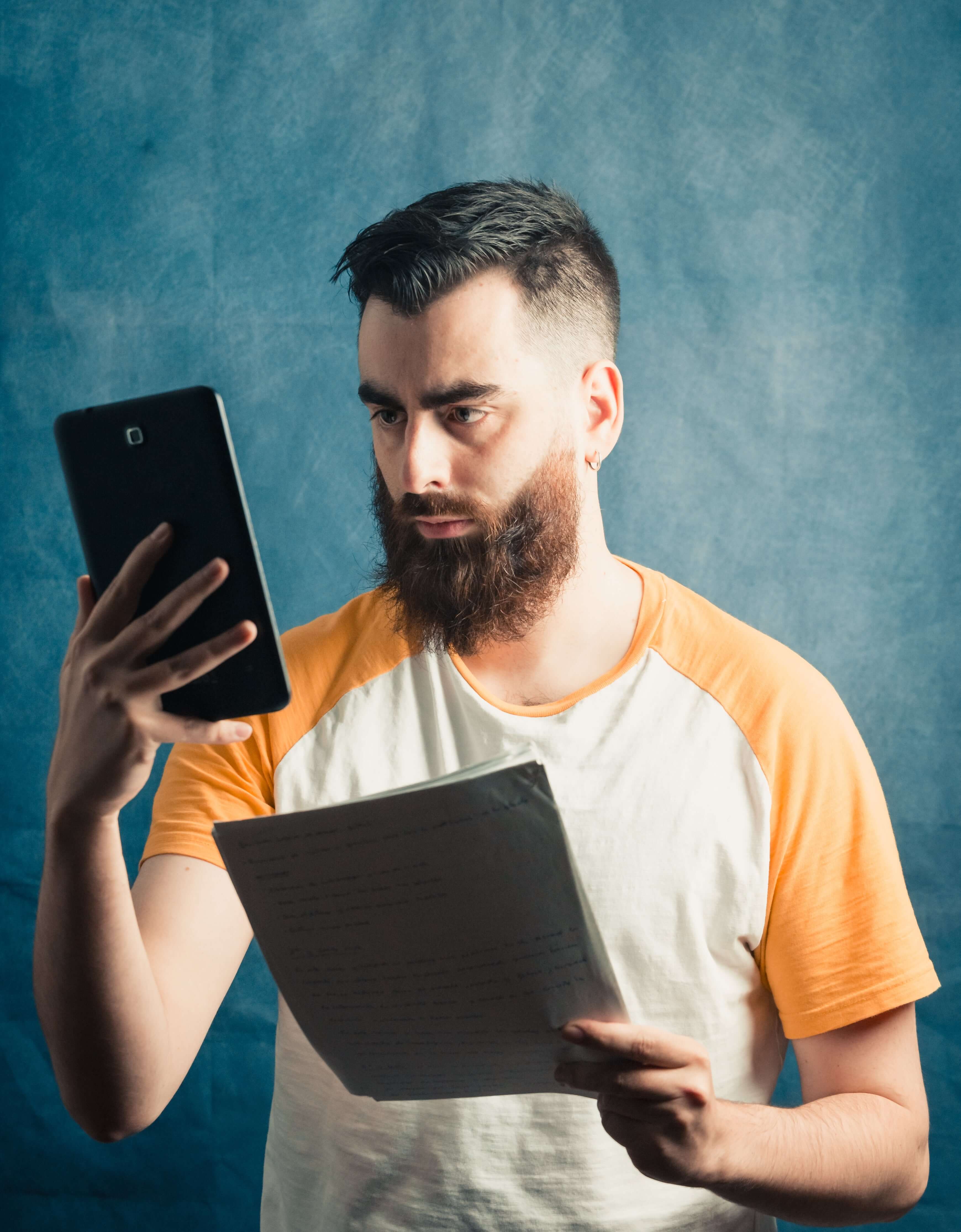 Man holding a tablet and a book against a blue background

