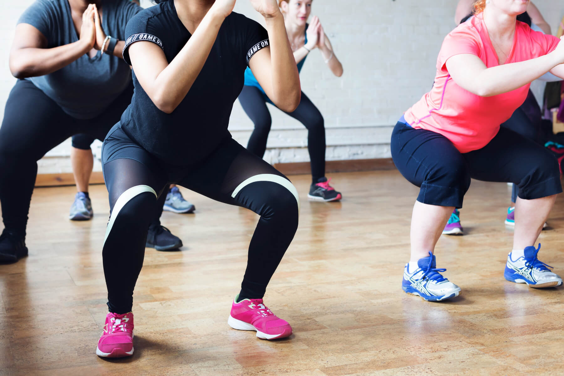 Group of people participating in a fitness class, performing squats on a wooden floor.
