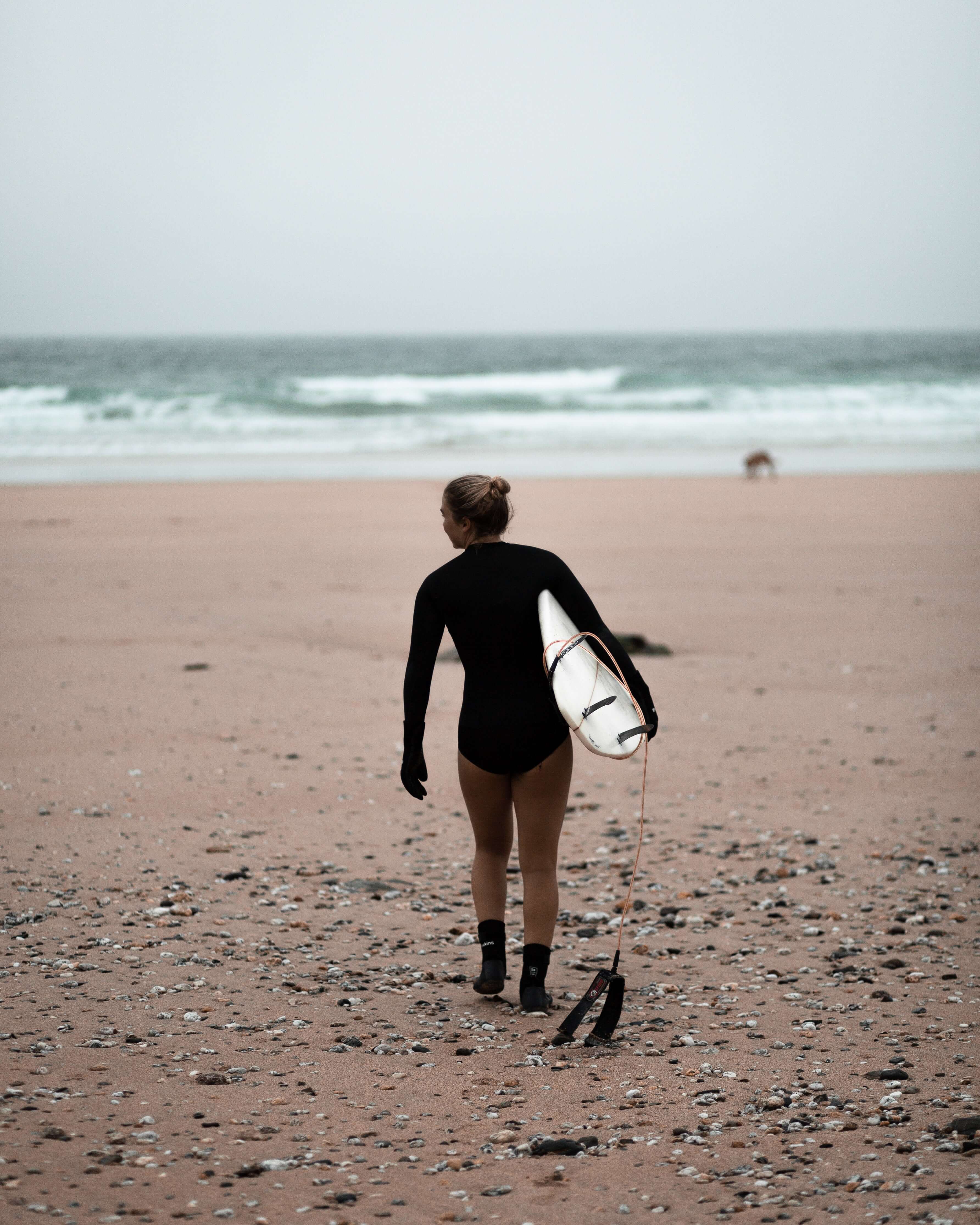 Person in a wetsuit walking on a beach with a surfboard
