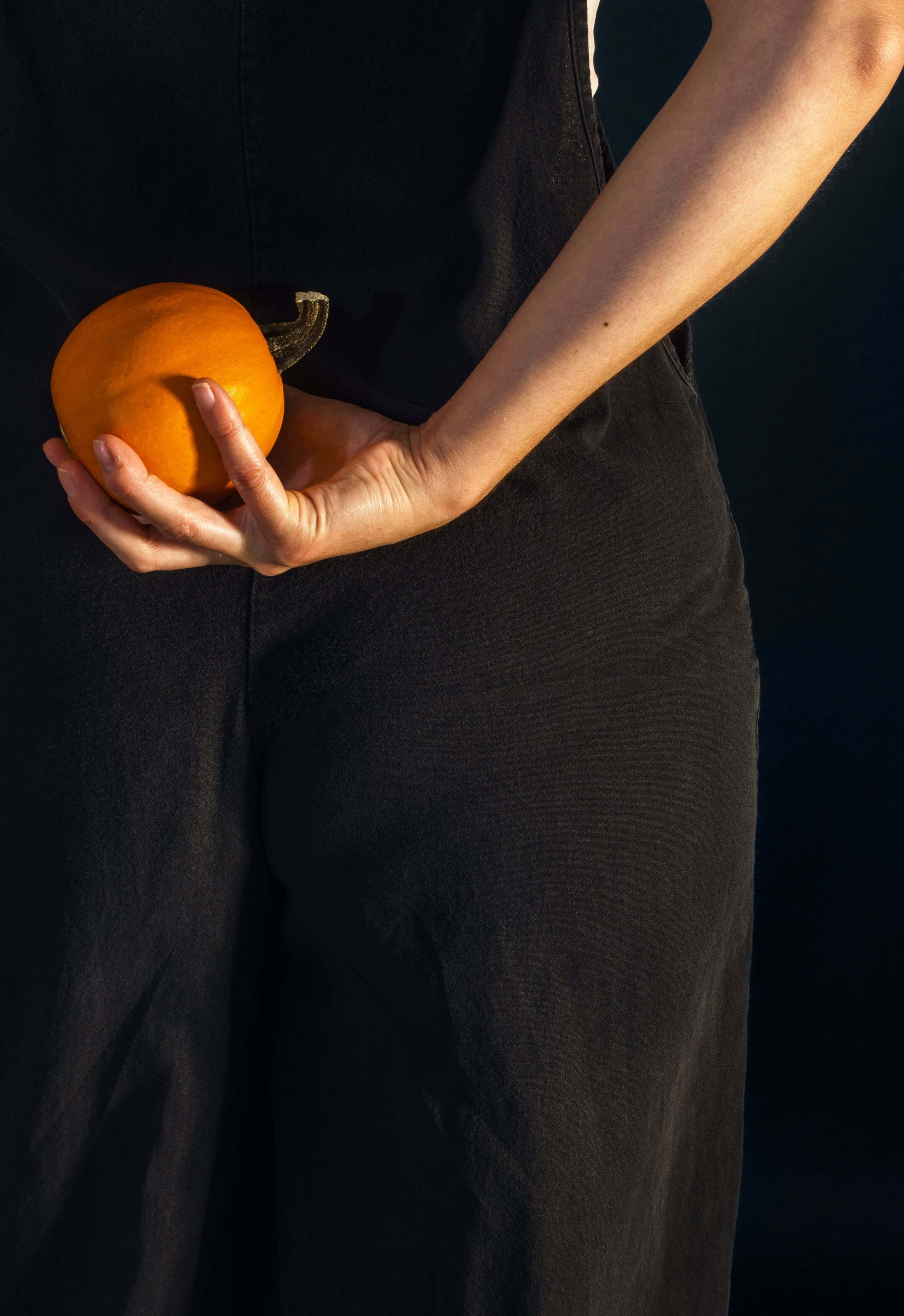 Person holding a small pumpkin against a dark background

