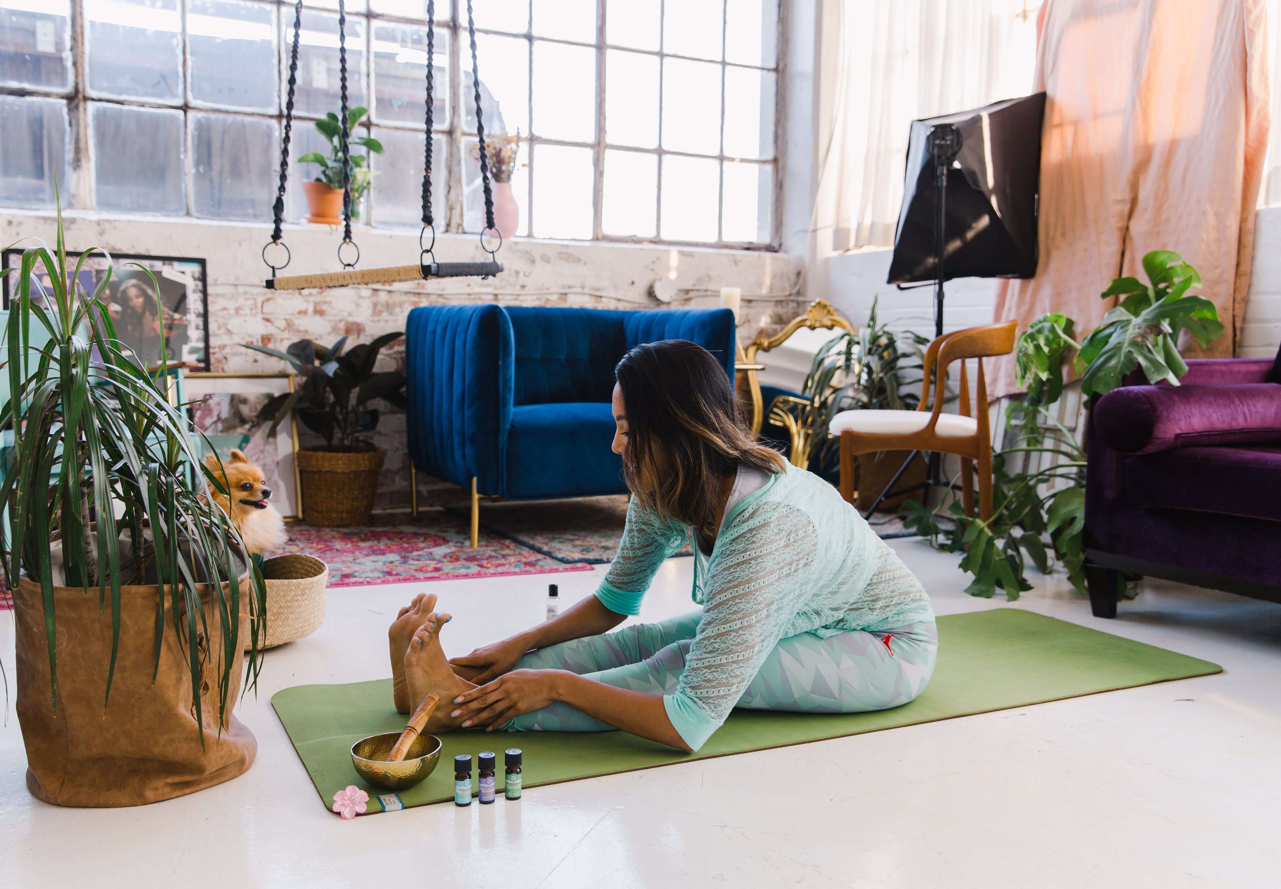 Woman sitting on a yoga mat in a cozy living room with plants and furniture.
