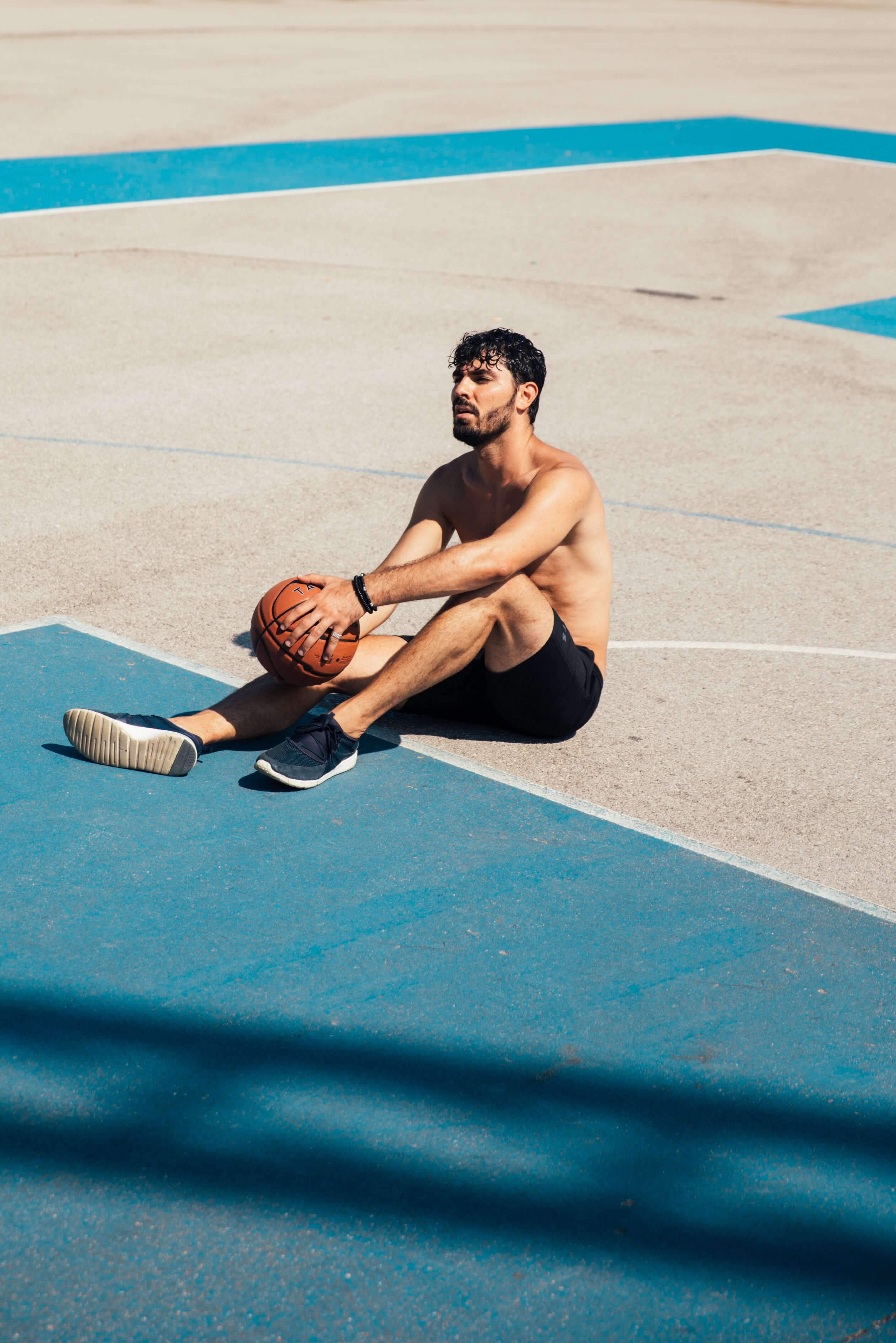 Man sitting on a basketball court holding a basketball
