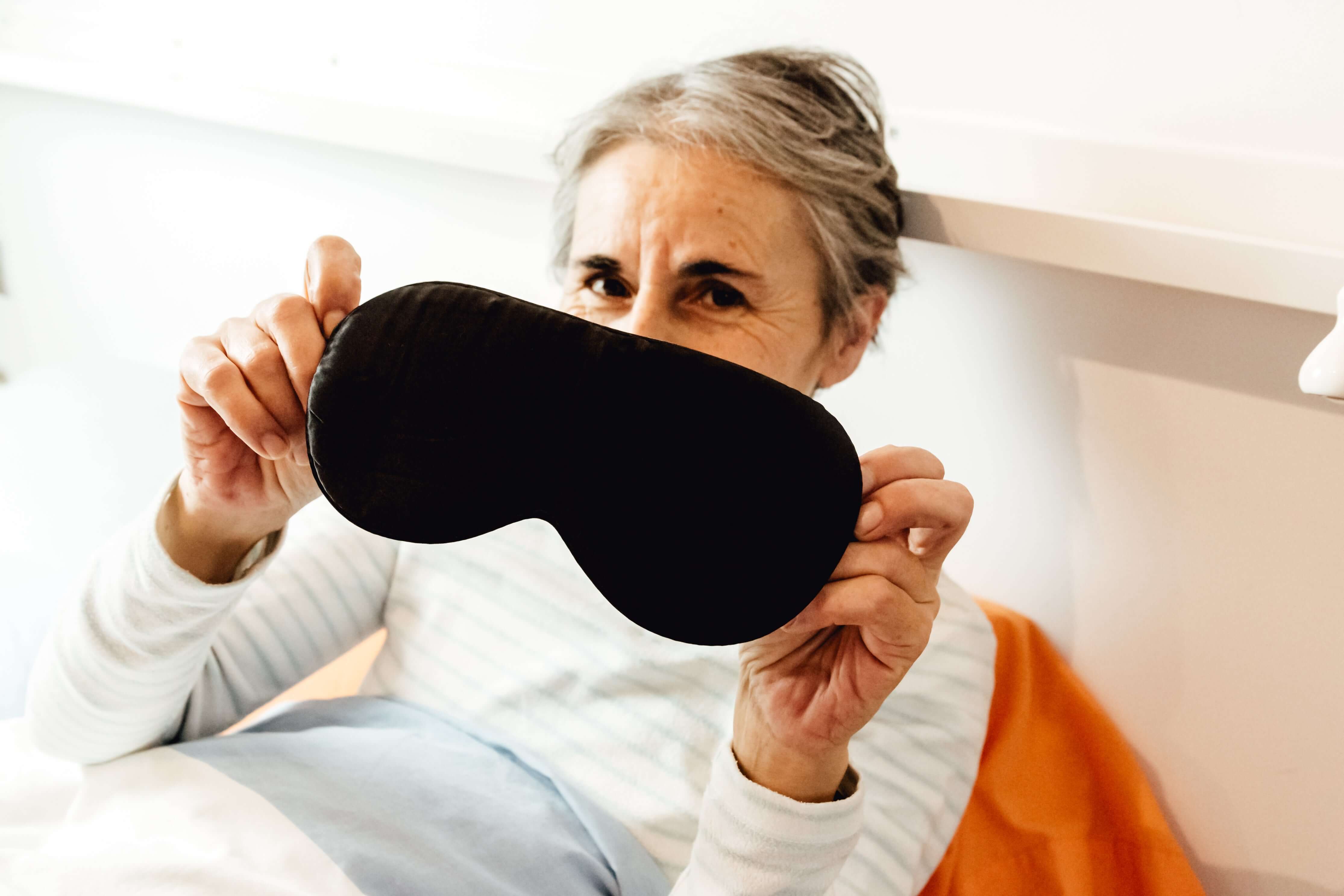 Woman holding a black sleep mask in front of her face
