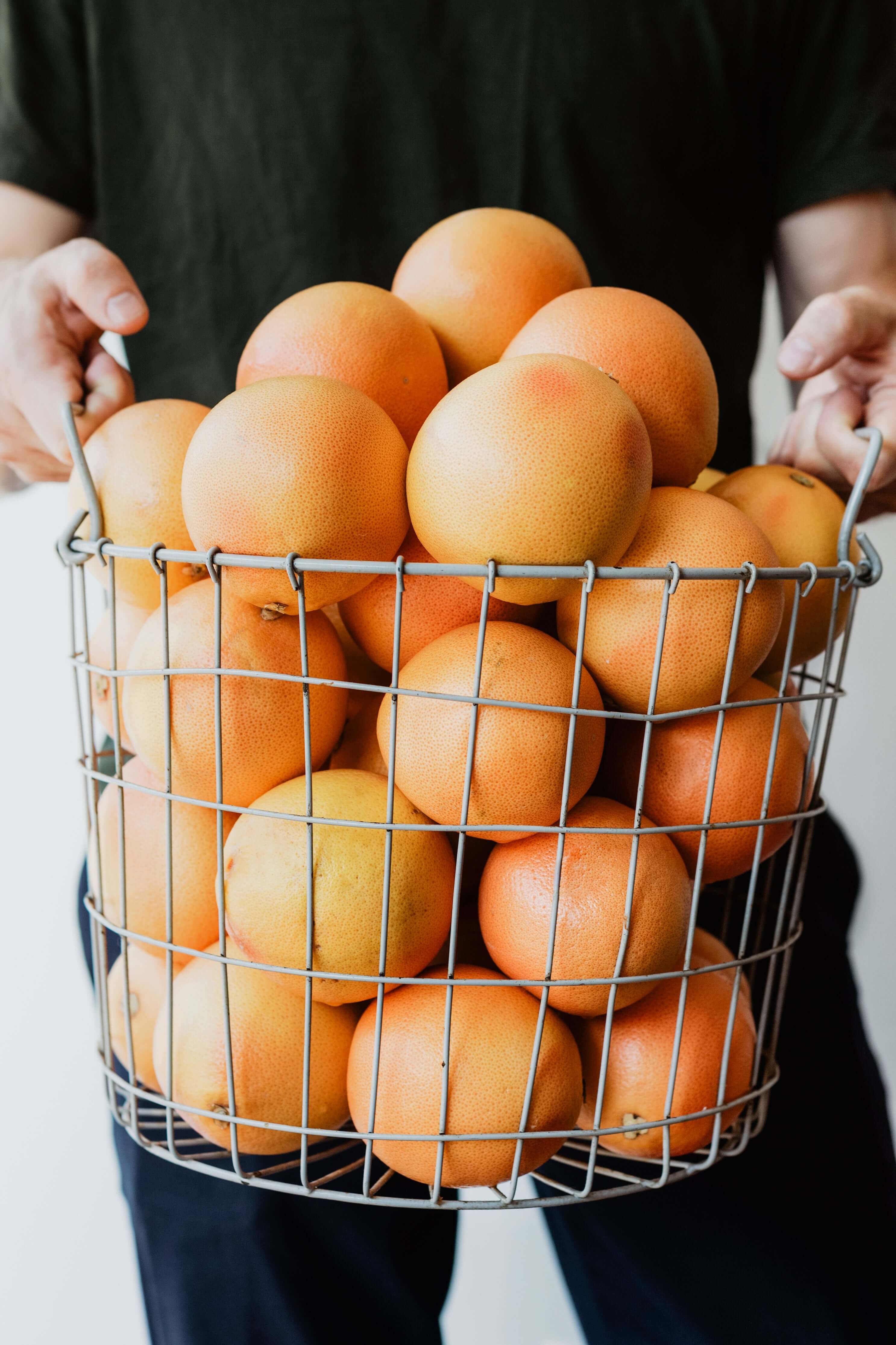 Basket of oranges held by a person with a neutral background
