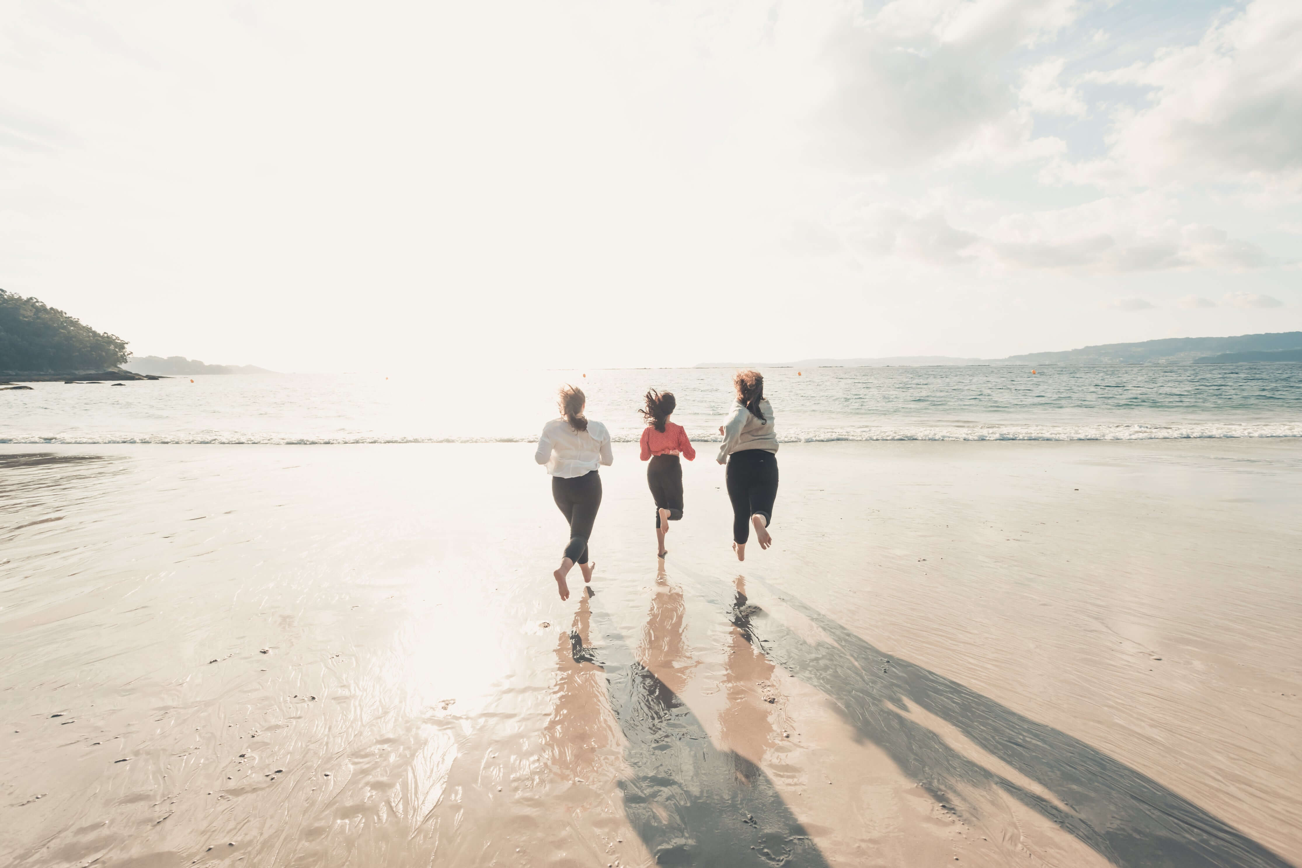 Three people walking on a beach with their shadows stretching on the sand.
