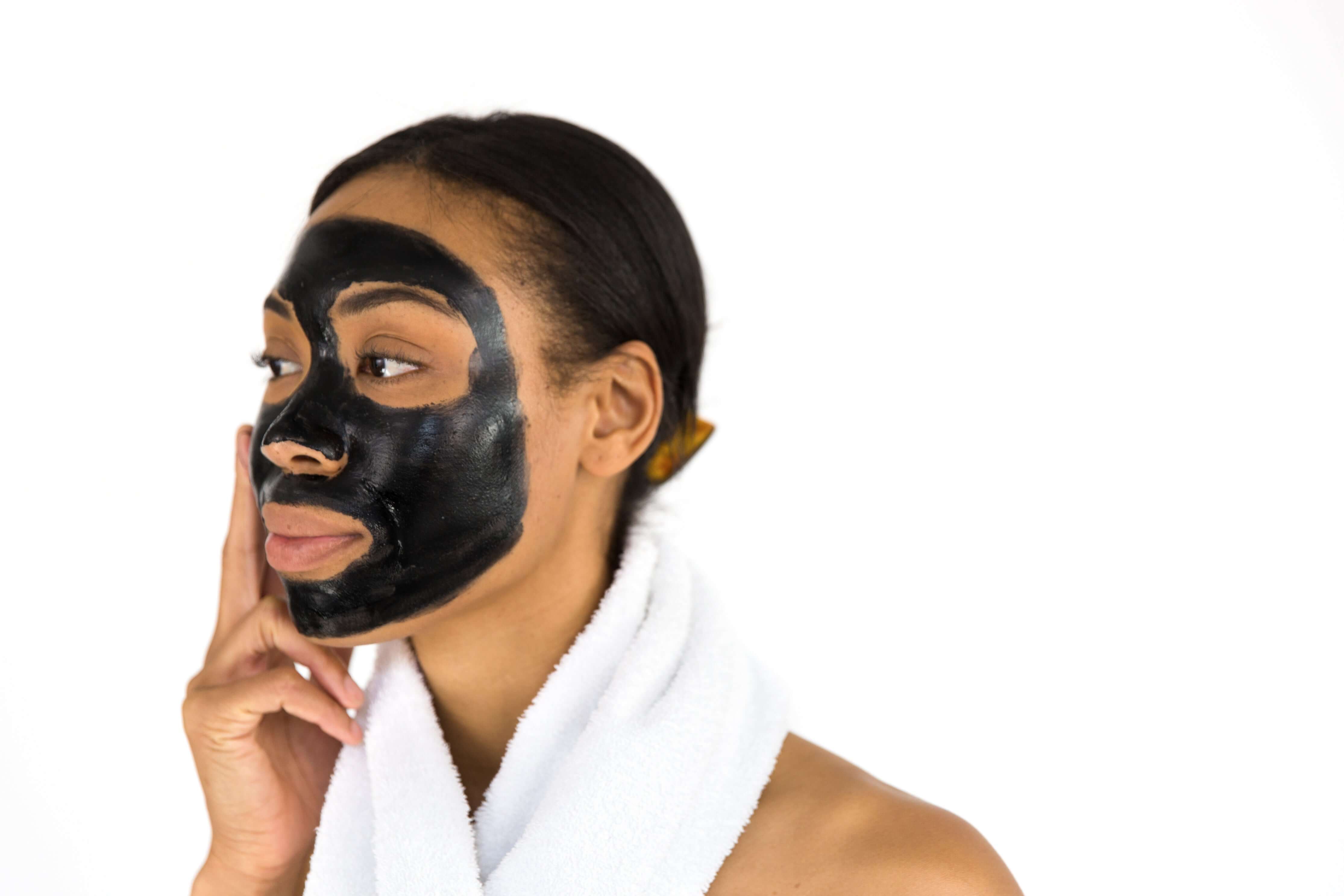 Woman wearing a black face mask with a white towel around her neck on a white background
