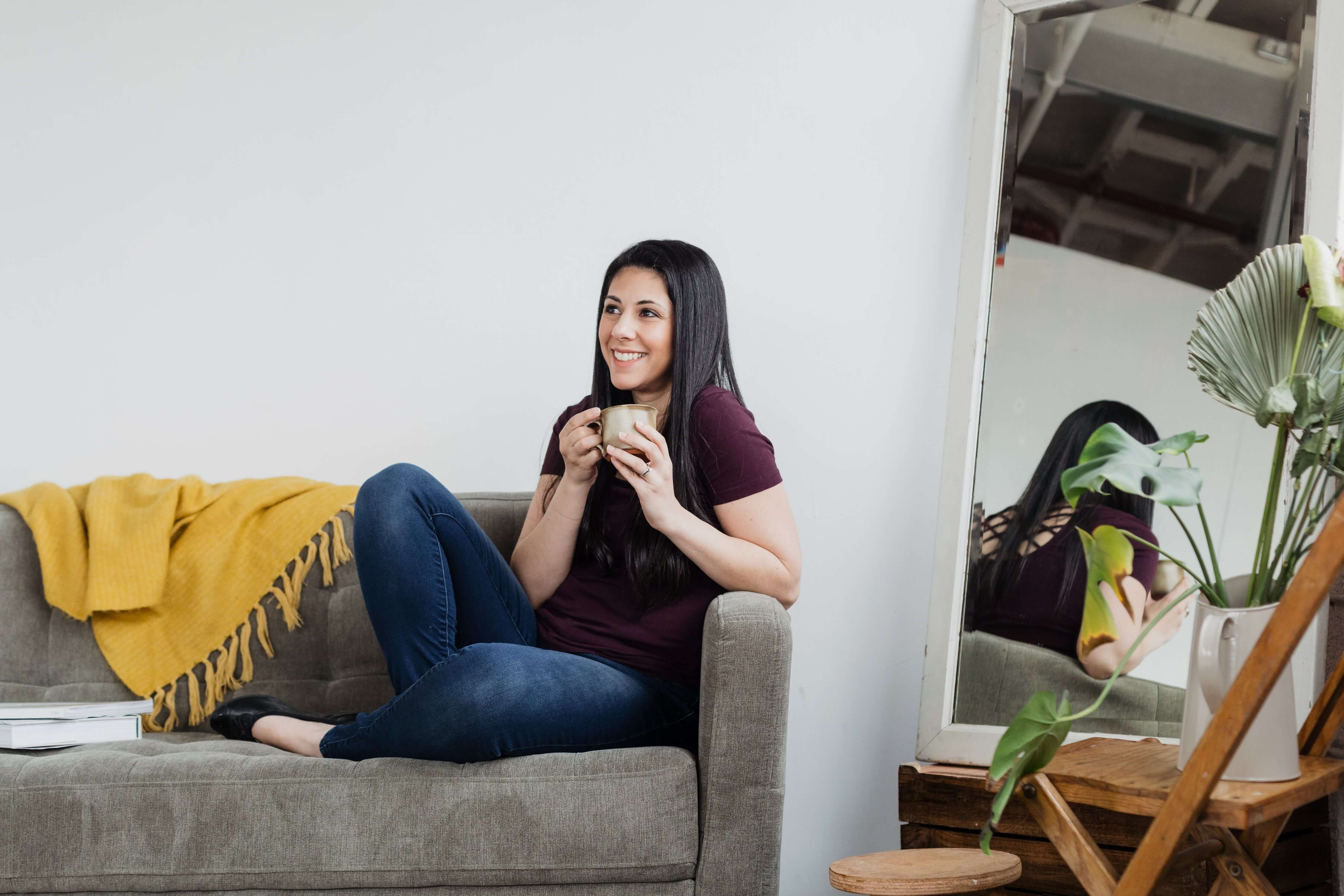 Woman sitting on a couch holding a mug in a cozy living room.
