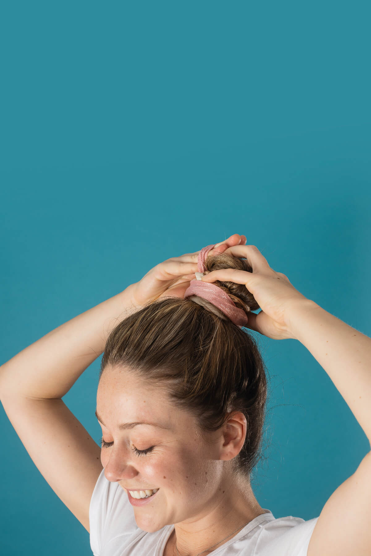 Woman tying her hair into a bun against a teal background
