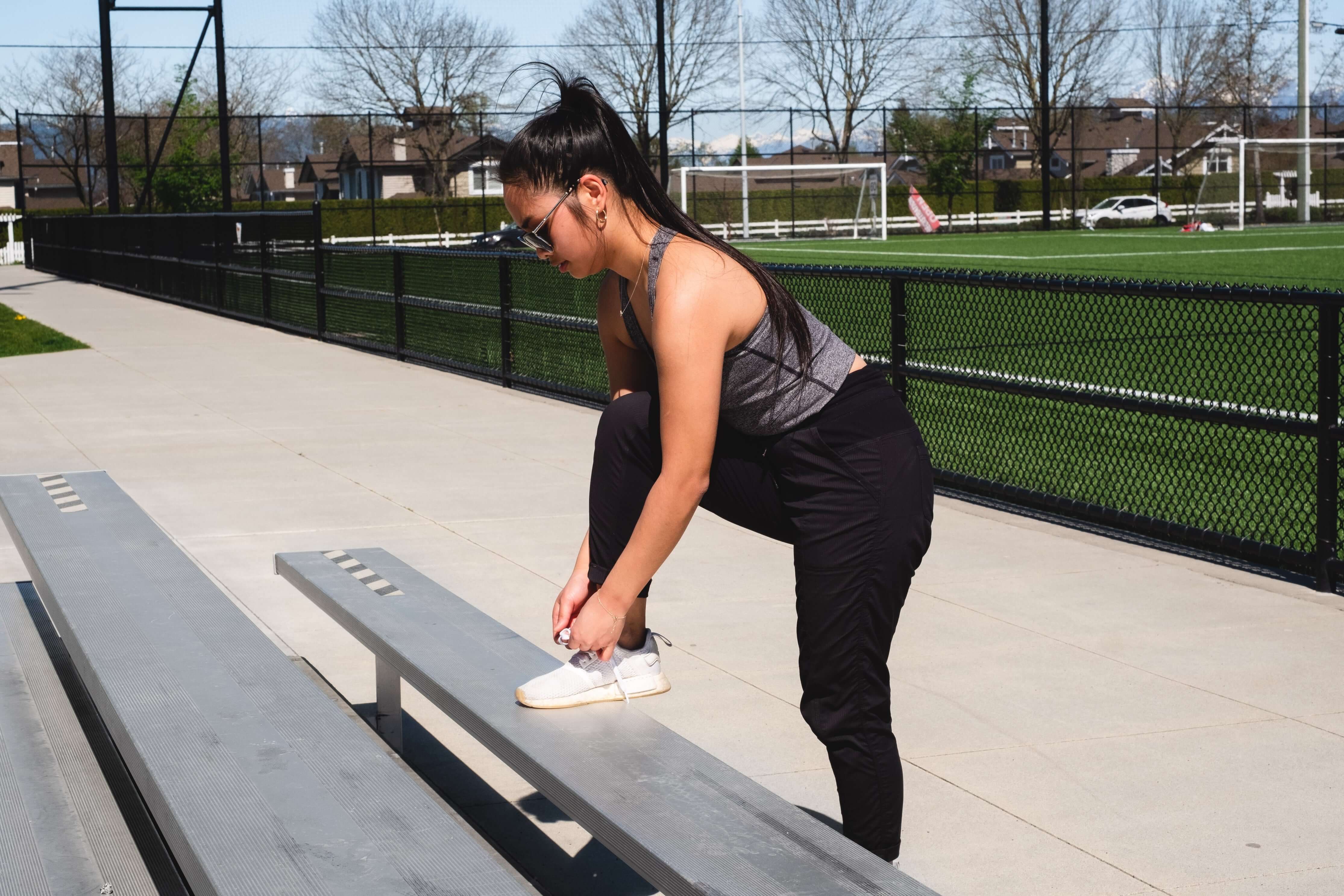 Woman tying her shoes on a bench in an outdoor setting
